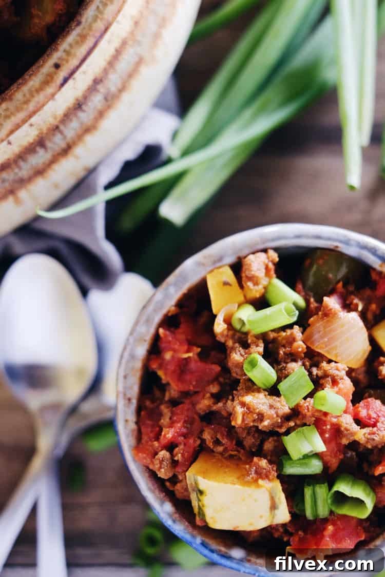 A close-up of a hearty bowl of Paleo Squash Chili, showcasing chunky pieces of winter squash, ground meat, and a rich, tomato-based broth.
