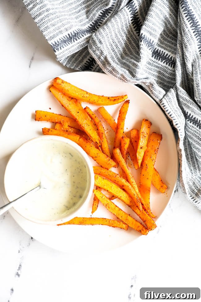 A beautifully presented plate of golden-brown oven-baked butternut squash fries, accompanied by a small ramekin of creamy ranch dressing, inviting a delicious dip.