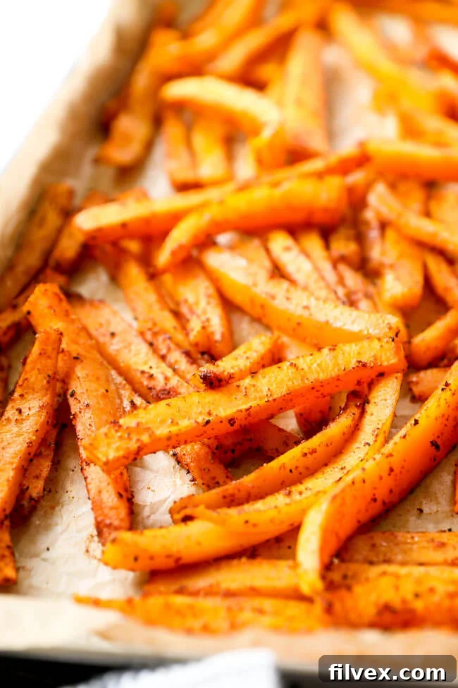 A close-up, angled view of perfectly oven-baked butternut squash fries spread out on a baking sheet, showcasing their crisp edges and golden-brown color.
