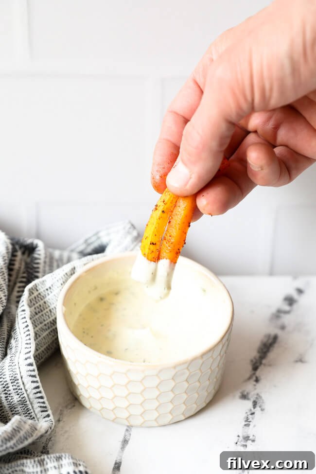 A close-up, angled shot capturing two crispy butternut squash fries being dipped into a creamy ranch sauce, emphasizing their golden color and the delicious act of dipping.