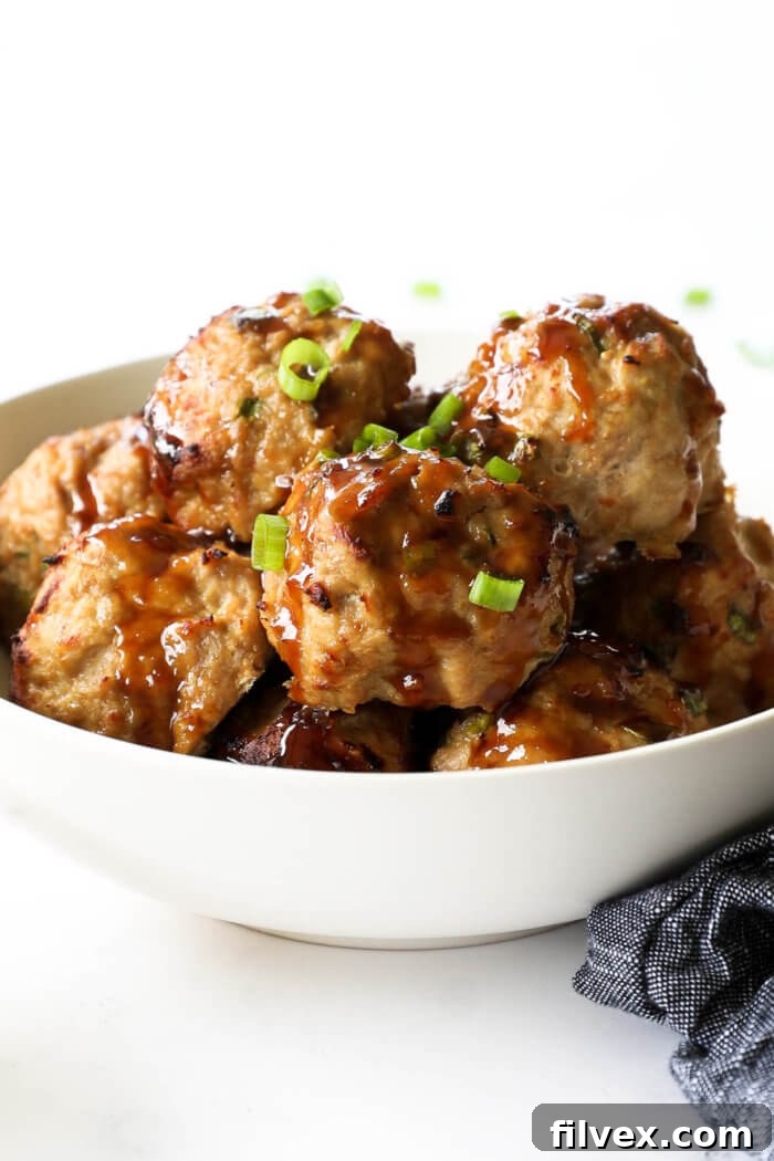 Close-up of golden-brown paleo teriyaki turkey meatballs piled in a rustic ceramic bowl, generously drizzled with a glossy, dark homemade teriyaki sauce and garnished with bright green chopped scallions, showcasing their appetizing texture and rich flavor.