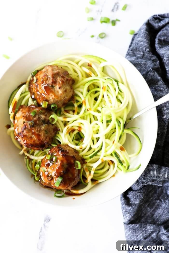 Overhead shot of vibrant teriyaki turkey meatballs served in a white bowl with spiralized zucchini noodles (zoodles), garnished with fresh green onions and sesame seeds, showcasing a healthy, low-carb meal option.