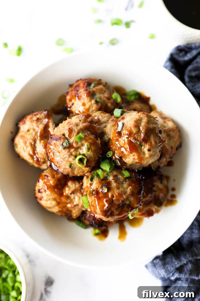 Overhead view of a bowl overflowing with perfectly baked teriyaki turkey meatballs, glistening with a generous coating of sticky, sweet, and savory teriyaki sauce, adorned with freshly chopped green onions for a pop of color and freshness.