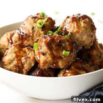 Angled image of a teriyaki turkey meatballs piled in a bowl with sticky teriyaki sauce drizzled on top. Garnished with chopped green onion.