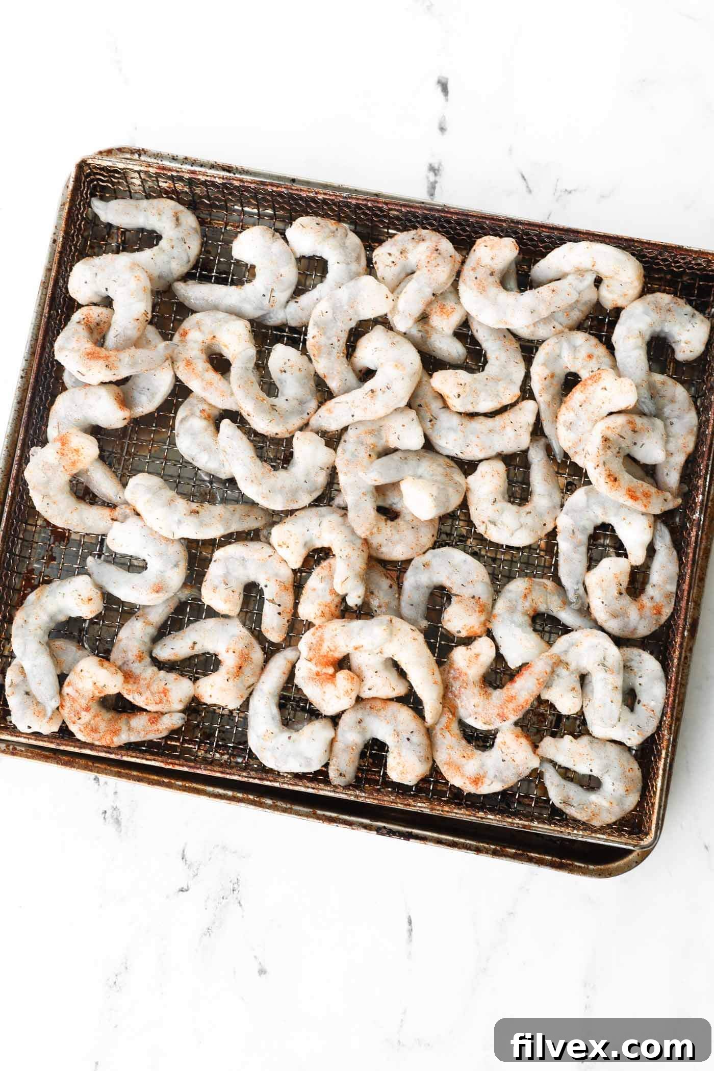 Seasoned frozen shrimp spread in a single layer inside an air fryer basket, ready for cooking.