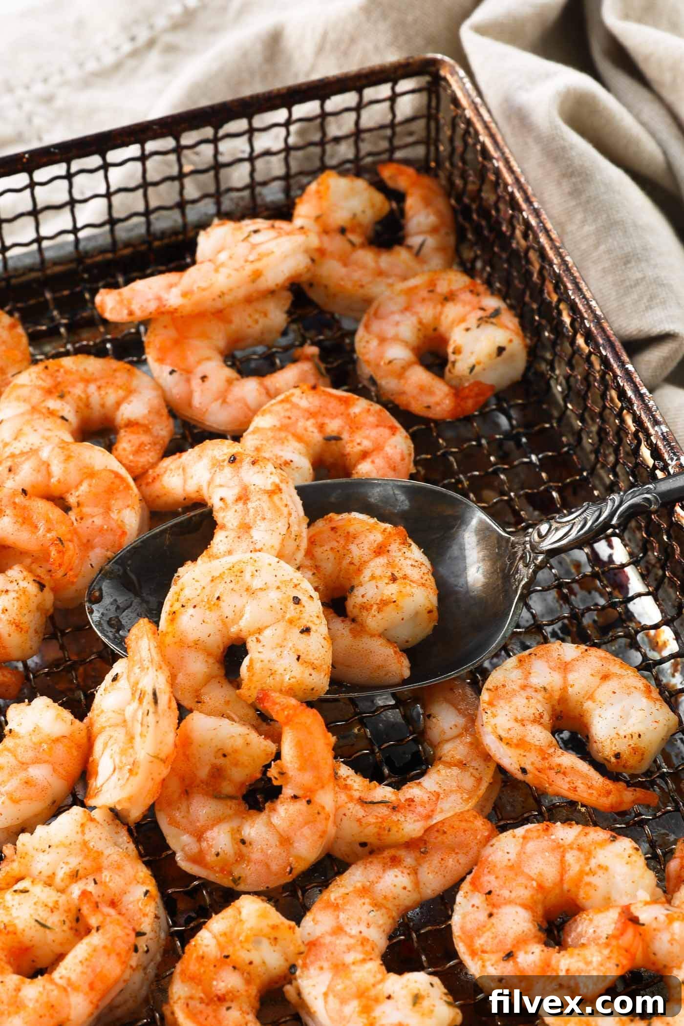 Close-up, angled shot of perfectly cooked air fryer shrimp in the basket, with a spoon scooping up a few pieces.