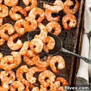 Air fryer shrimp after cooking in the air fryer basket with a serving spoon scooping a few pieces up.