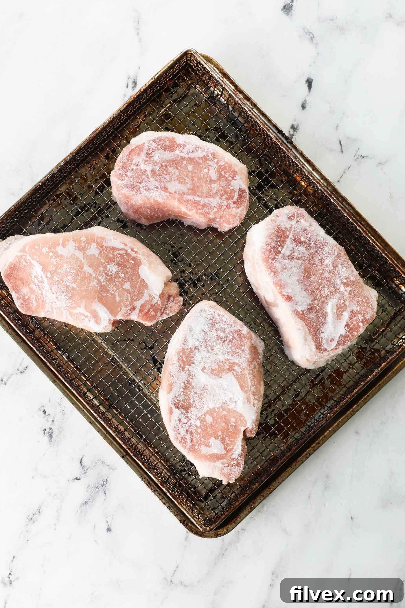 Frozen pork chops placed in an air fryer basket, ensuring good air circulation