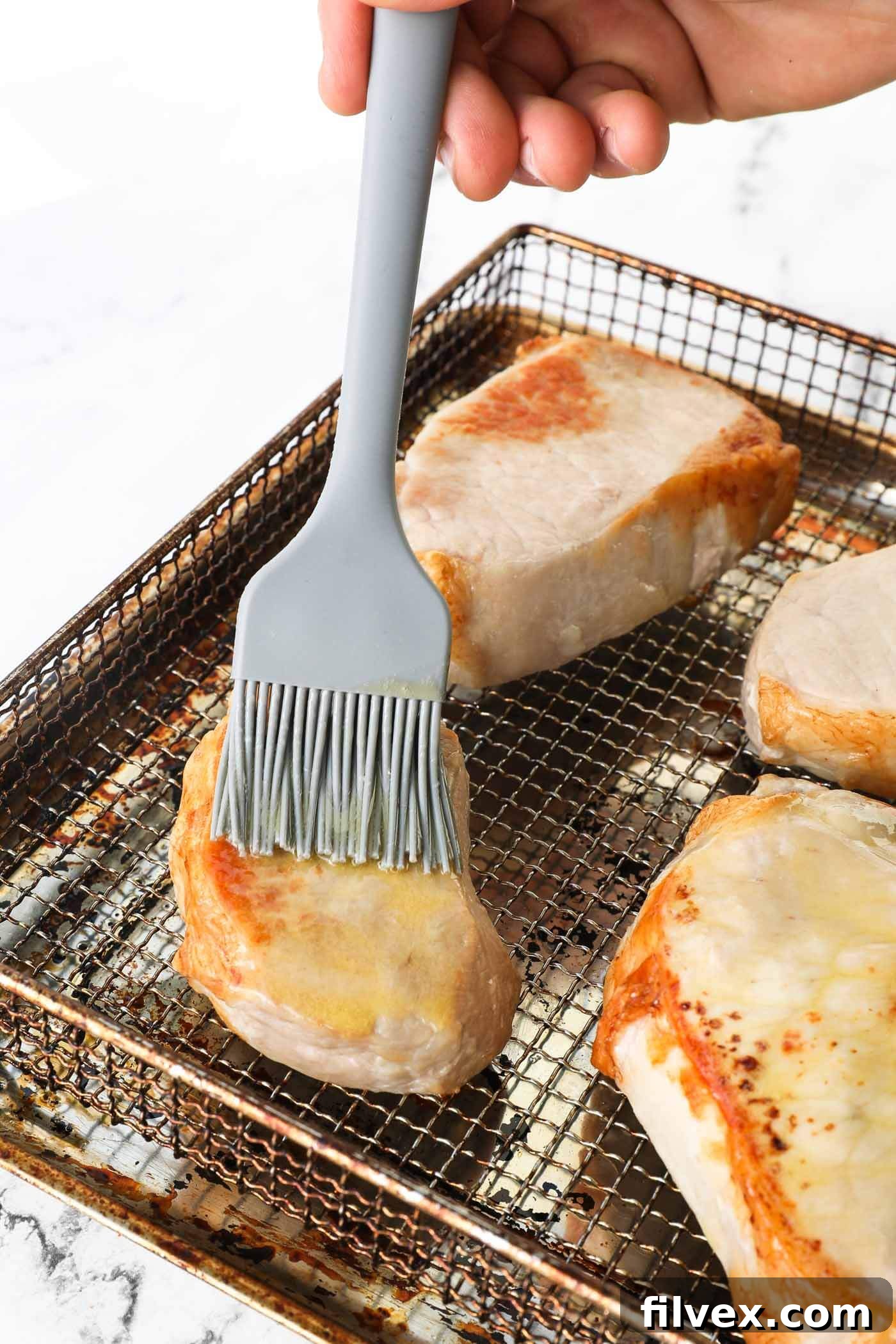 Pork chops in air fryer after initial cooking, being brushed with melted butter