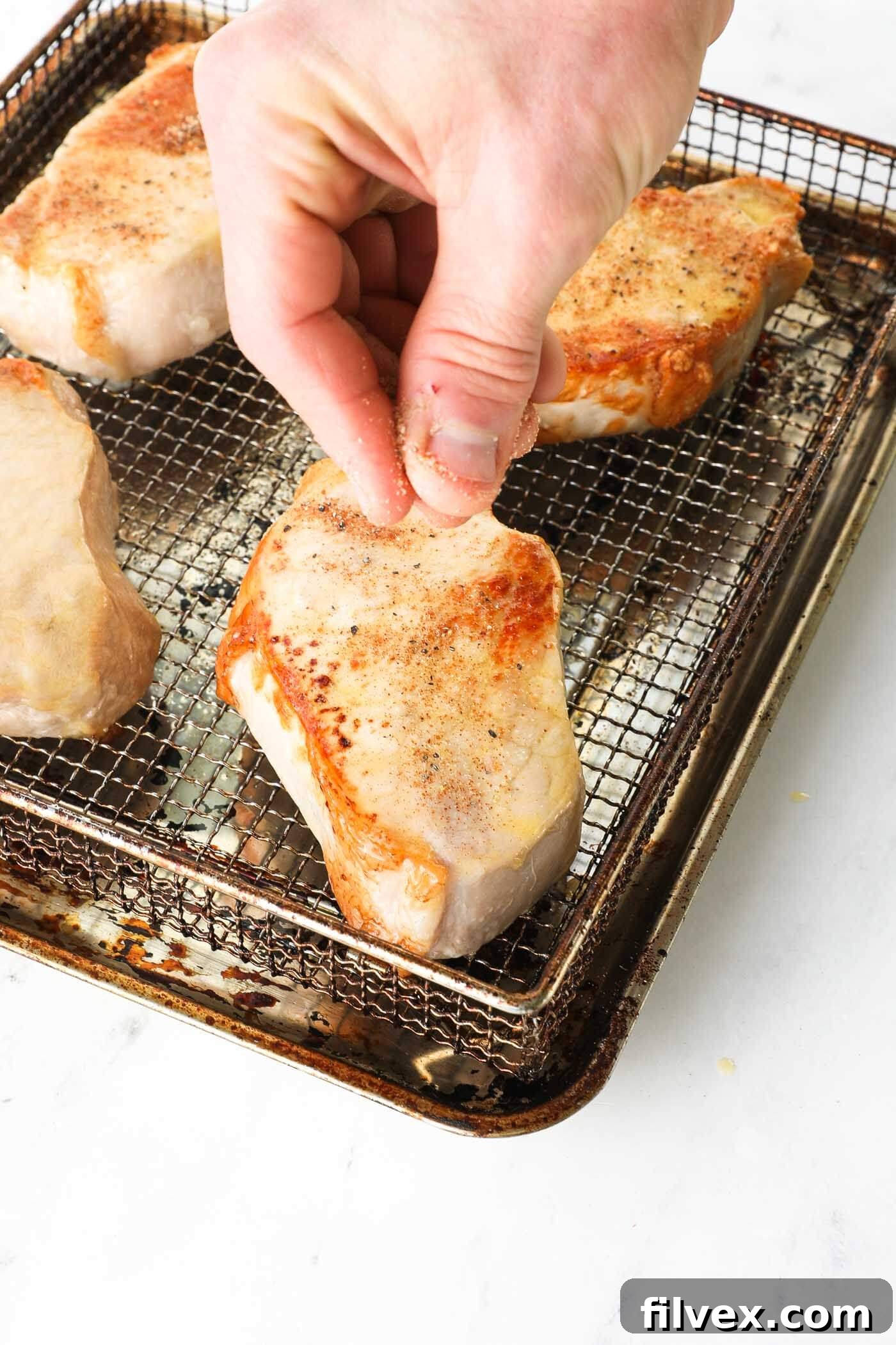 Pork chops being seasoned liberally with a spice rub after being brushed with butter