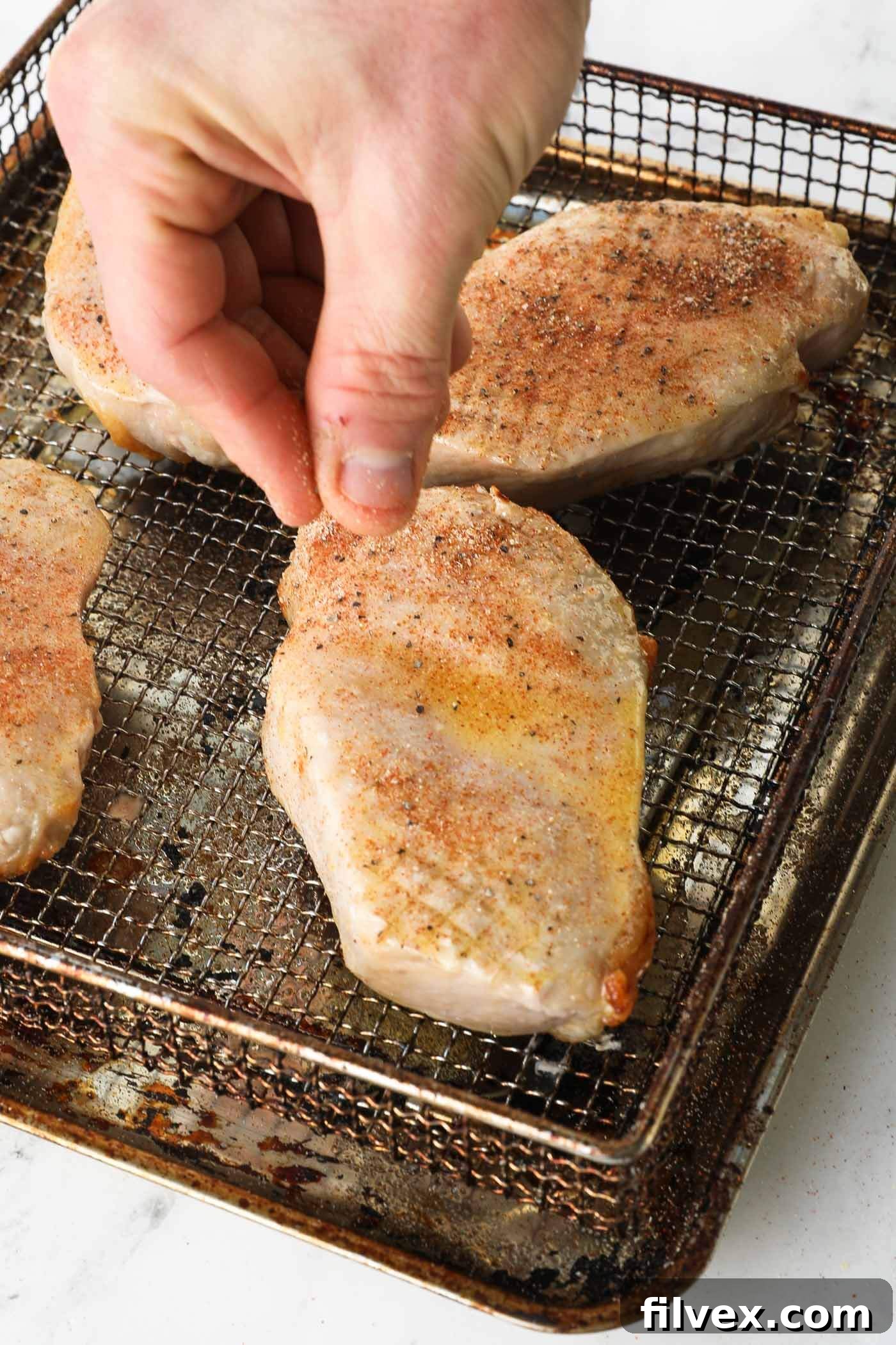 Pork chops flipped over, being brushed with butter and seasoned on the second side