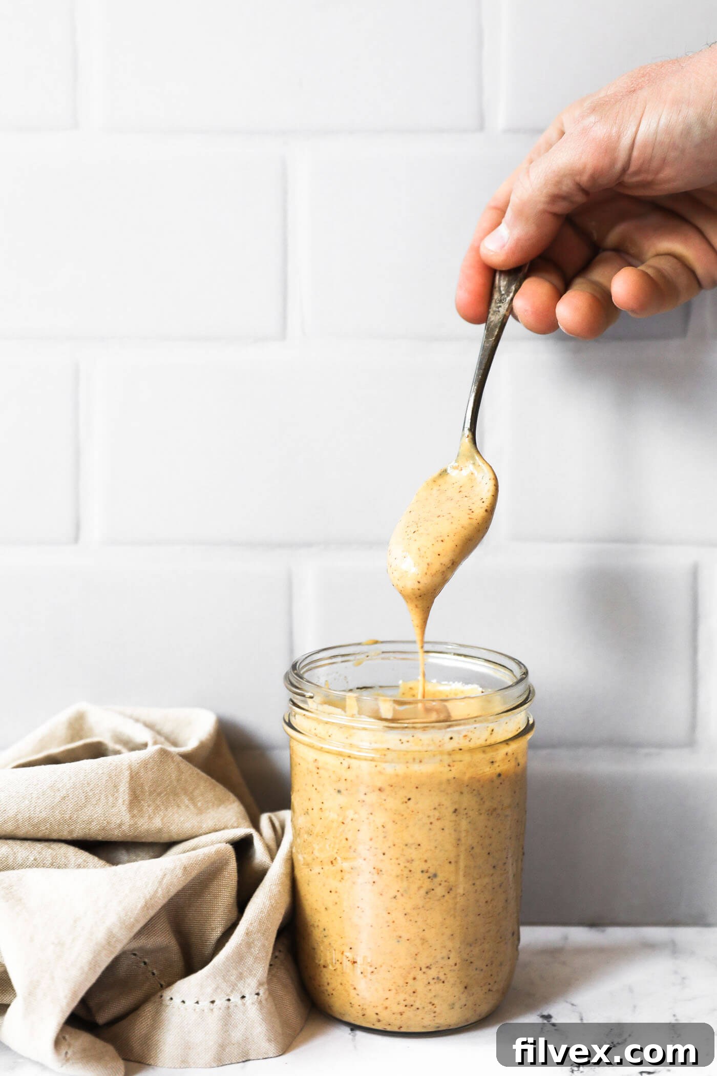 A hand pulling a spoon dipped in the chili aioli sauce out of a mason jar. The sauce is dripping off the spoon and back into the jar. 
