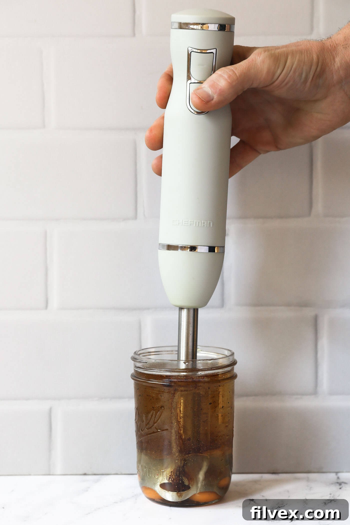 An immersion blender in a mason jar, about to be turned on to emulsify the ingredients.