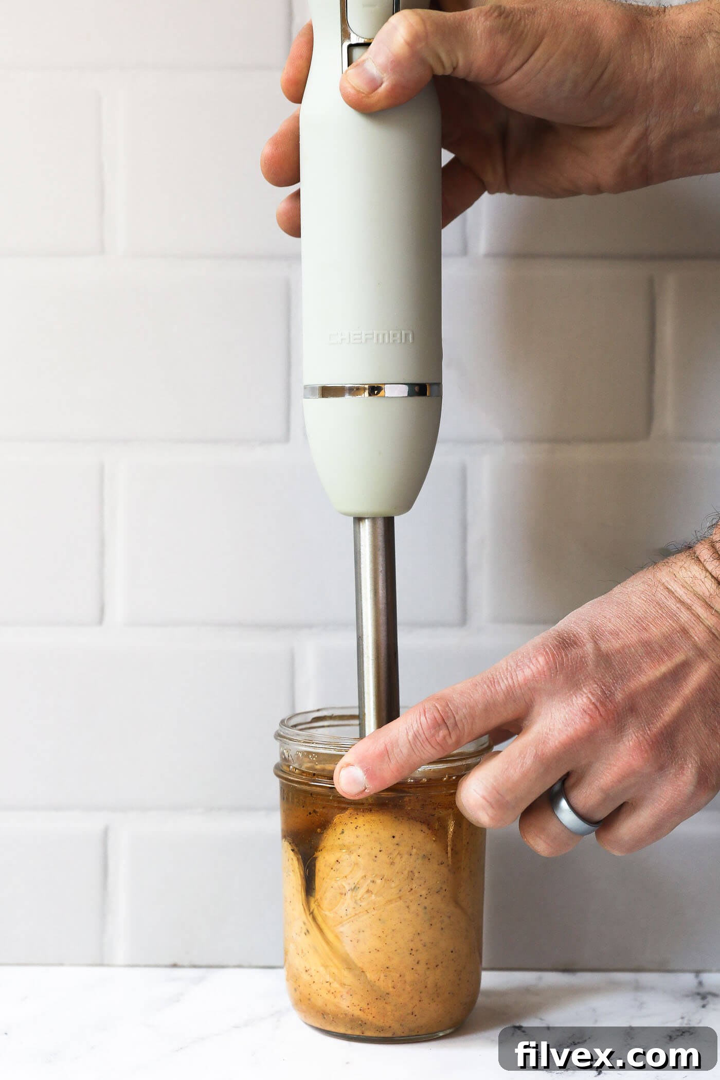 Someone using an immersion blender to emulsify a homemade chili aioli in a mason jar. The sauce is not quite fully emulsified yet.