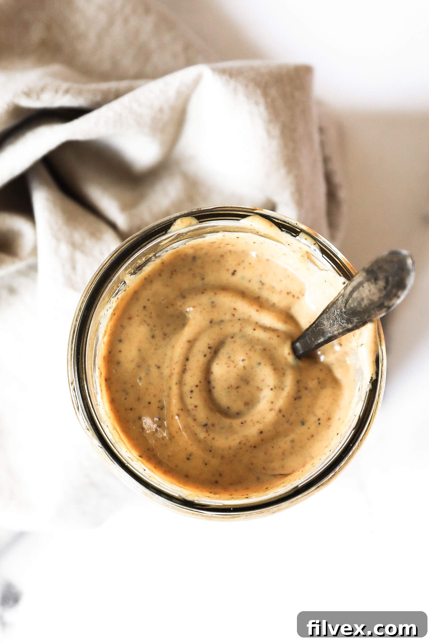 Overhead image of homemade aioli sauce in a mason jar with a spoon in the jar.