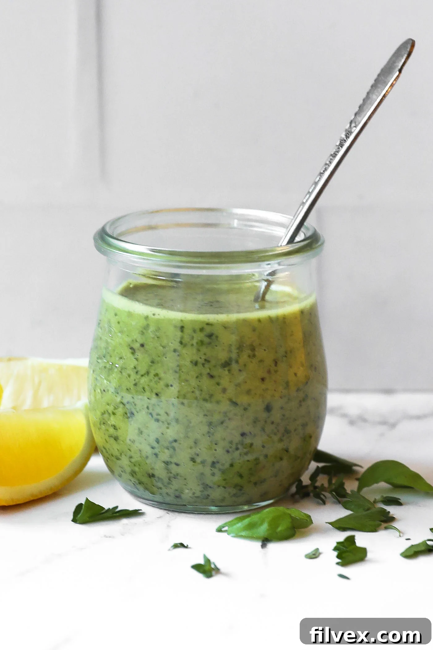 Vibrant lemon herb sauce in a clear glass jar, with fresh lemons and herbs scattered around, showcasing its freshness.