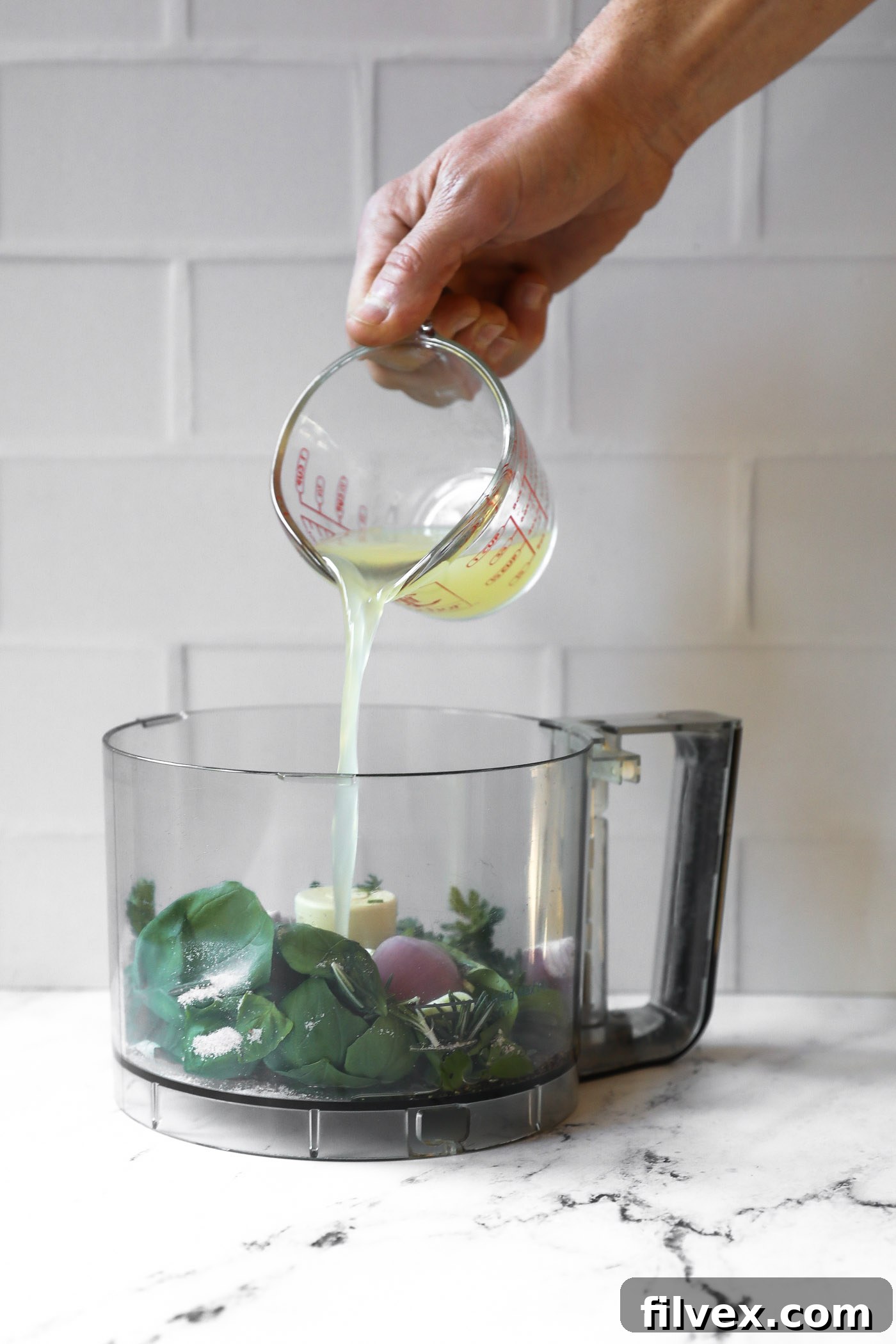 All fresh ingredients for lemon herb sauce, including lemons, parsley, basil, and garlic, placed into a high-powered blender or food processor.