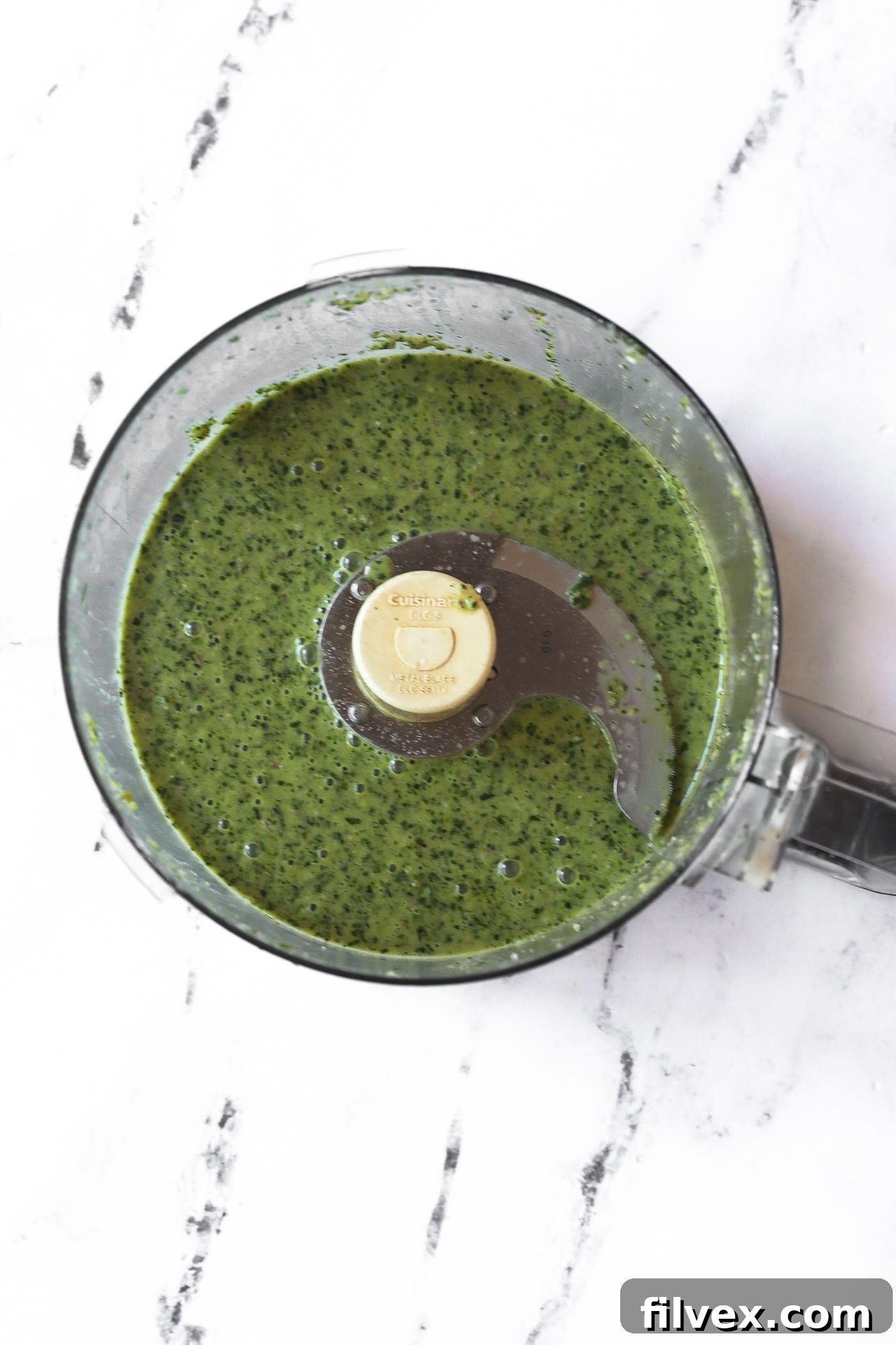 Lemon herb sauce being blended in a food processor until smooth, showing a vibrant green liquid.