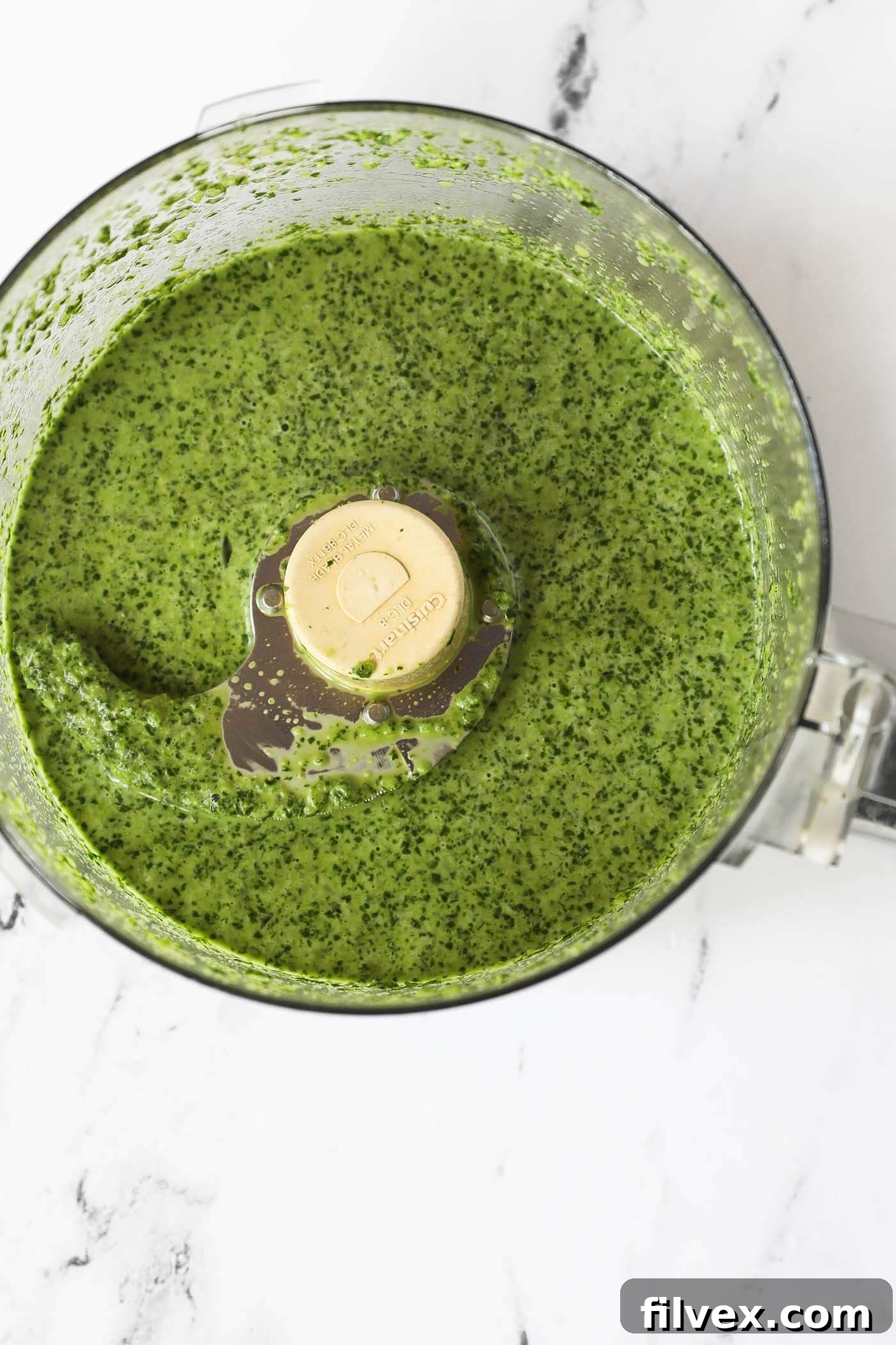 Garlicky cilantro lime sauce being blended in a food processor, showing a smooth, vibrant green consistency.