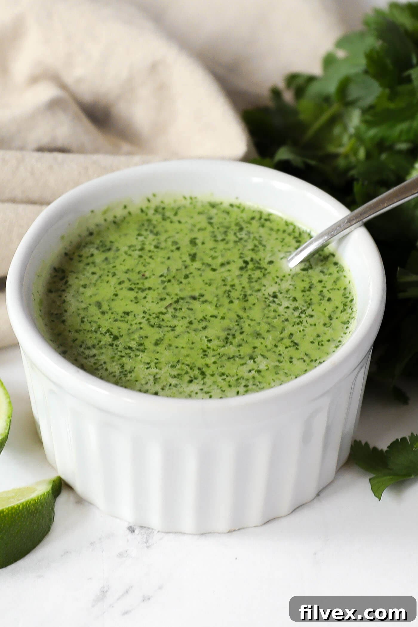 Close-up of the garlicky cilantro lime sauce in a ramekin, showing its vibrant green color and smooth texture, with fresh cilantro and lime in the background.