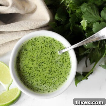Overhead shot of fresh cilantro lime sauce in a ramekin with a spoon coming out and fresh cilantro and lime wedges