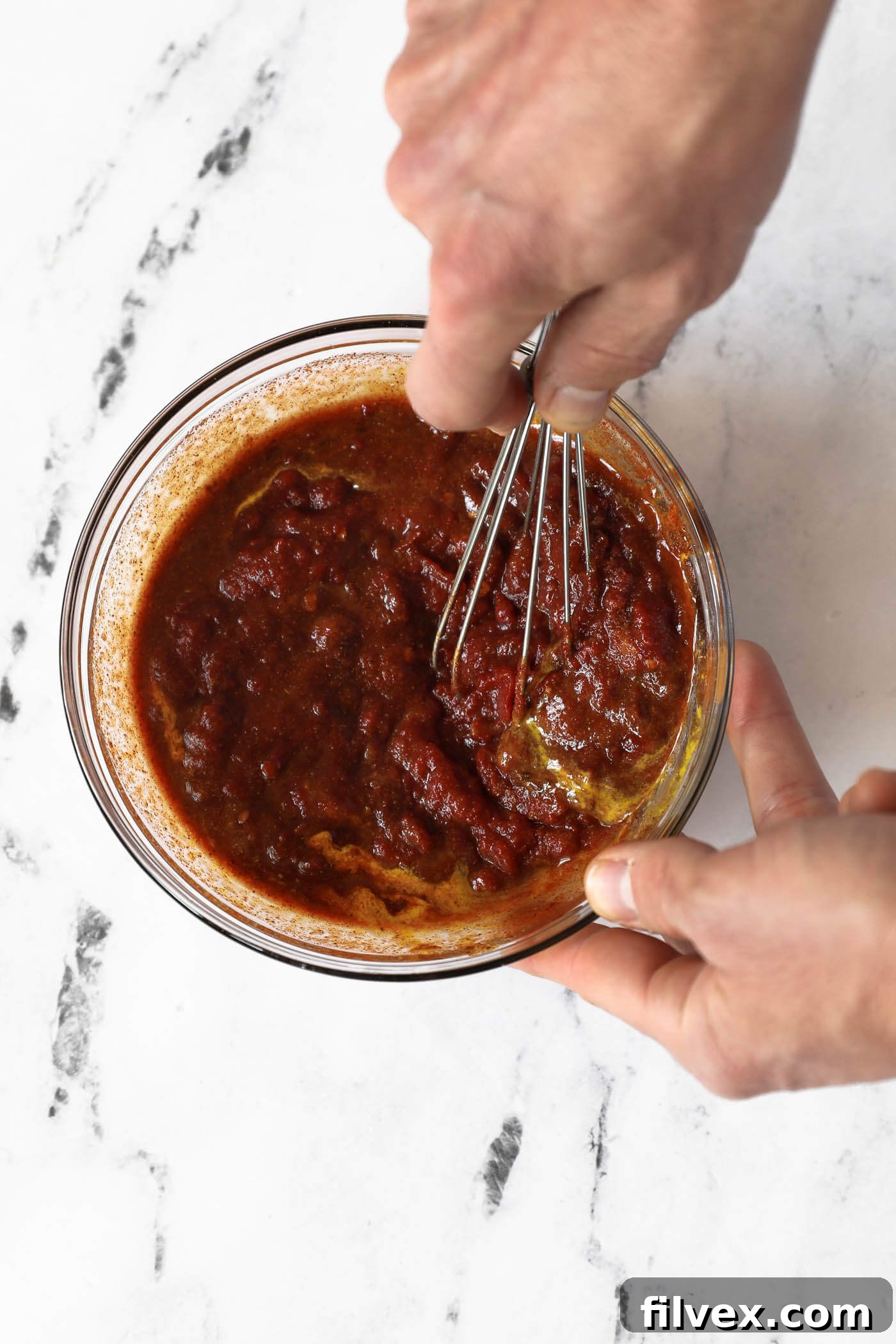 Hands whisking chipotle BBQ sauce ingredients together in a bowl.