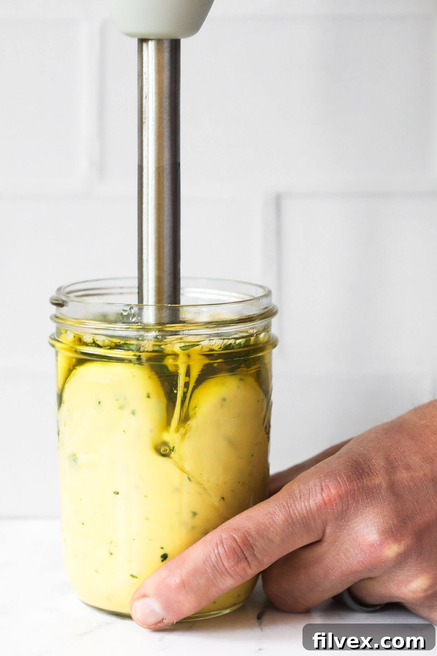 Cilantro lime aioli emulsifying in a mason jar as the immersion blender makes its way up the jar. The aioli is starting to thicken and turn creamy.