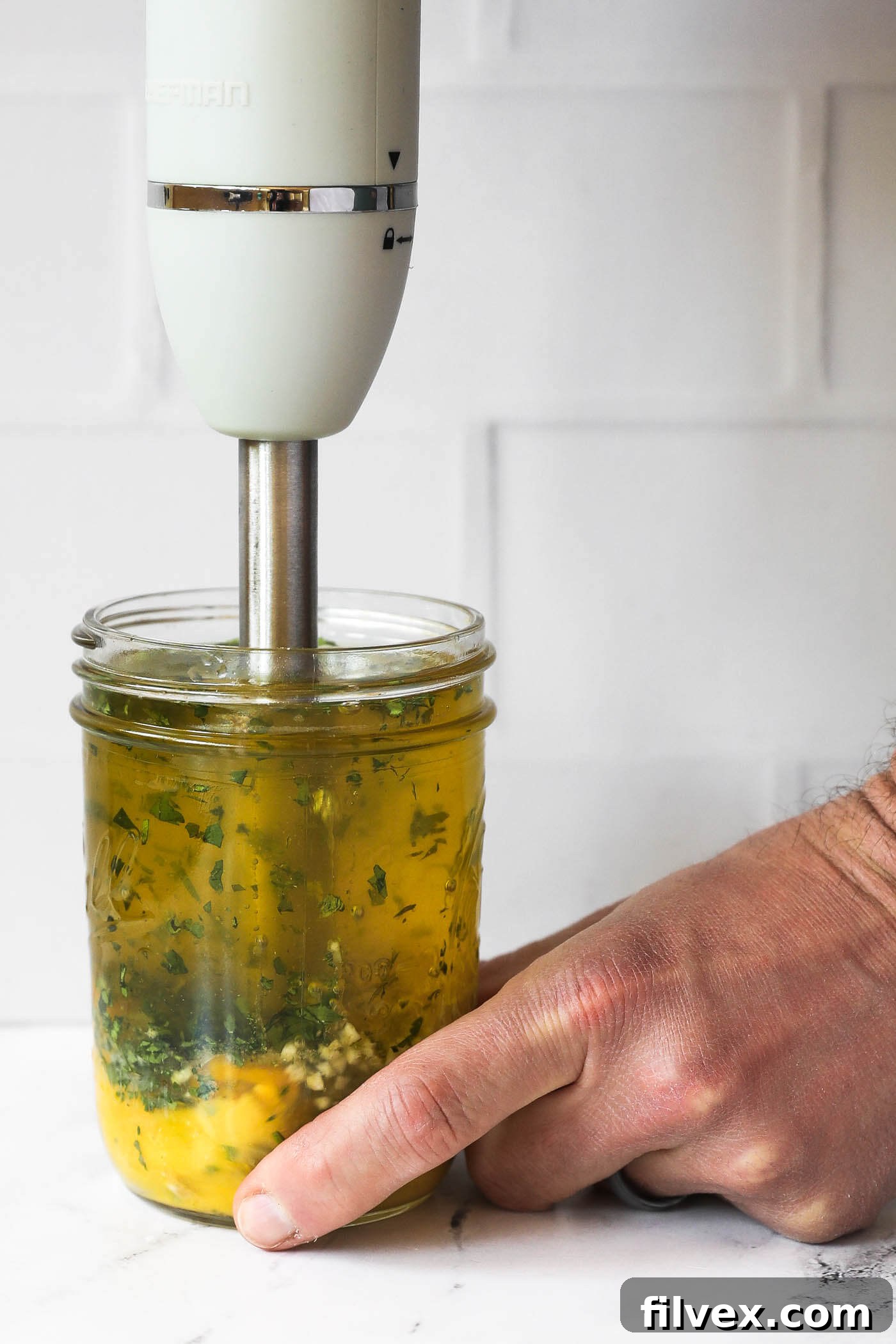 Someone carefully placing an immersion blender into a mason jar filled with all the ingredients for cilantro lime aioli, ready to blend.