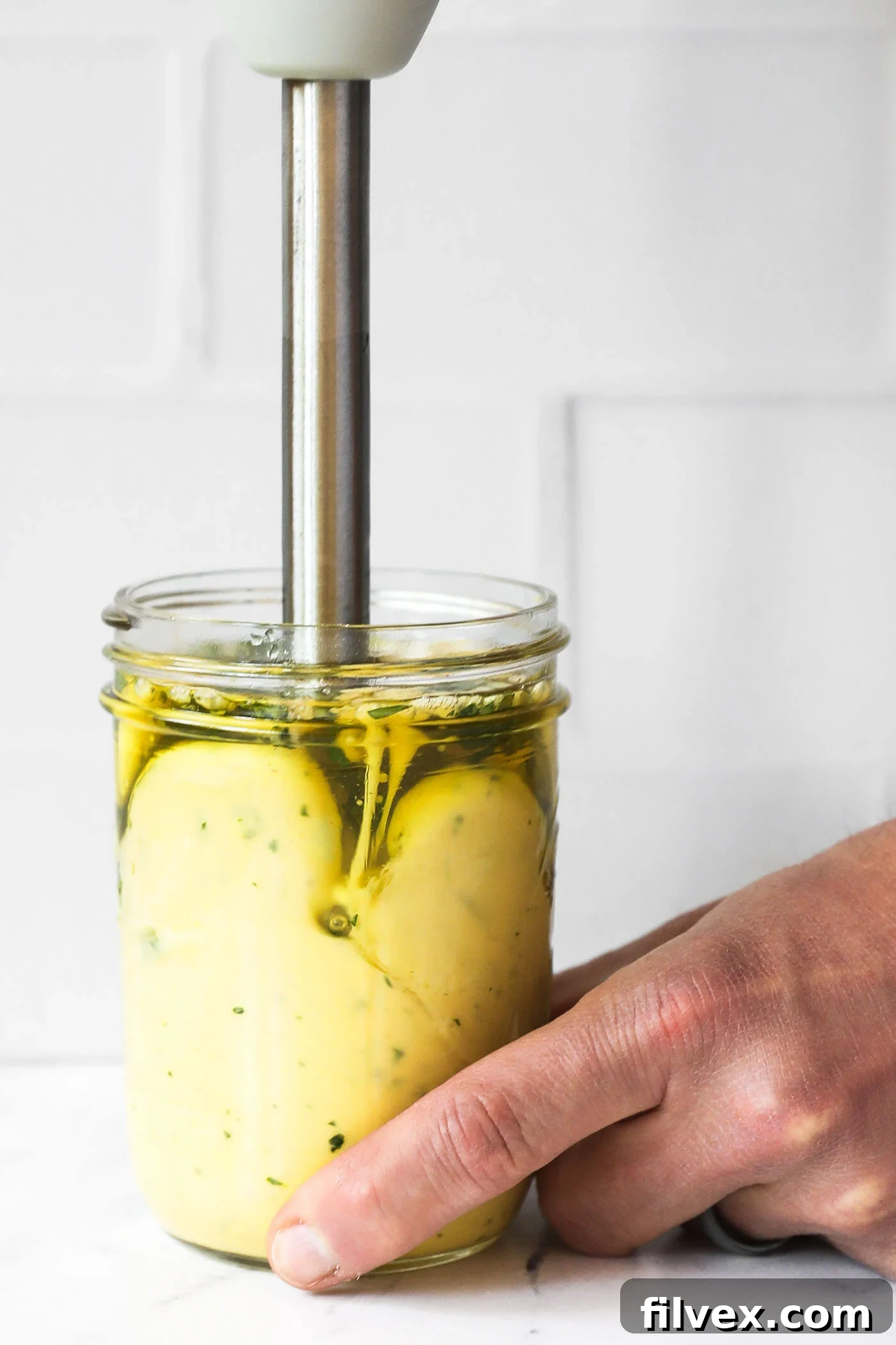 Close-up of vibrant green cilantro lime aioli emulsifying in a mason jar with an immersion blender. The bottom layer is visibly thicker and creamier.