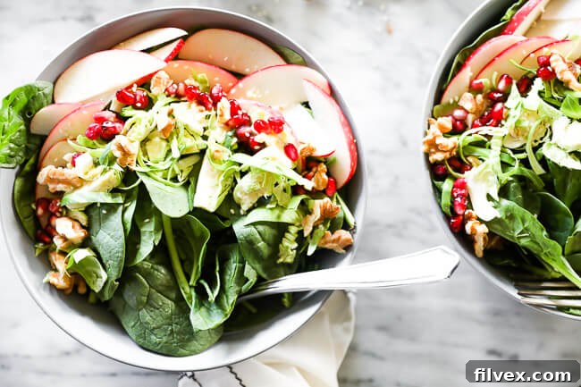 Two bowls of vibrant apple walnut spinach salad, with forks ready to enjoy. Crisp apples, fresh spinach, and crunchy walnuts are visible.