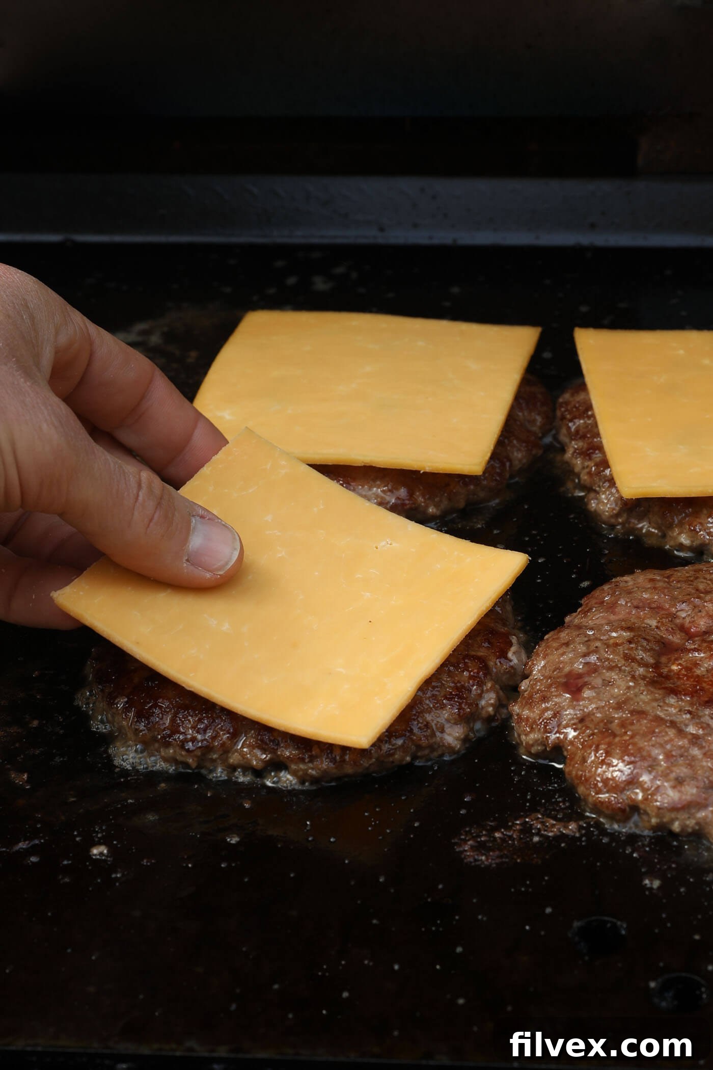 Adding cheese to smash burgers on a griddle