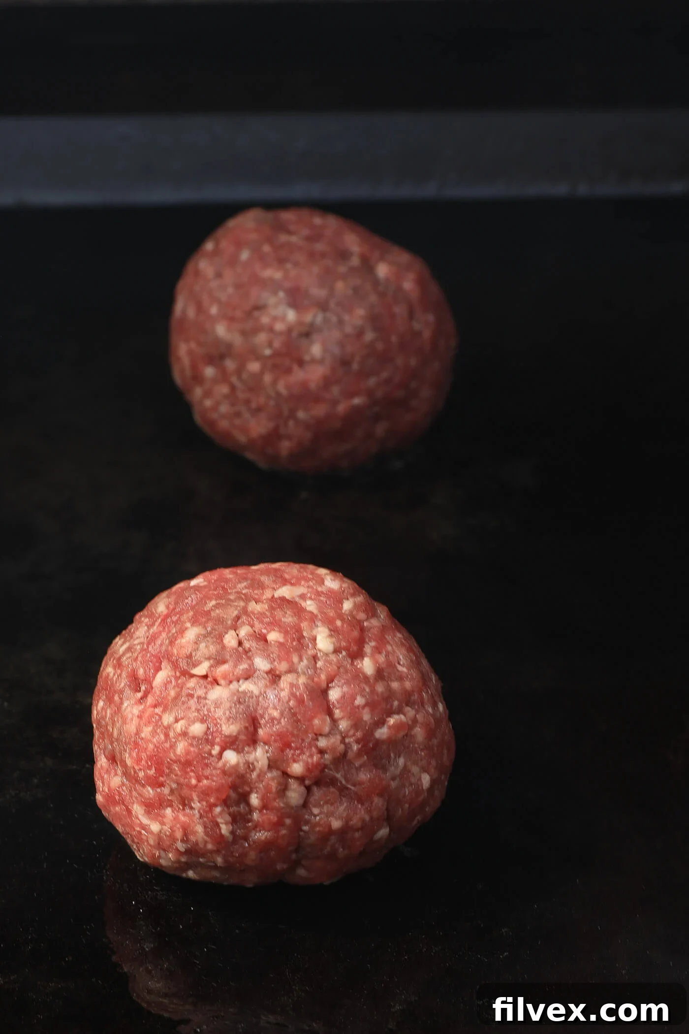 Beef balls searing on a griddle before smashing