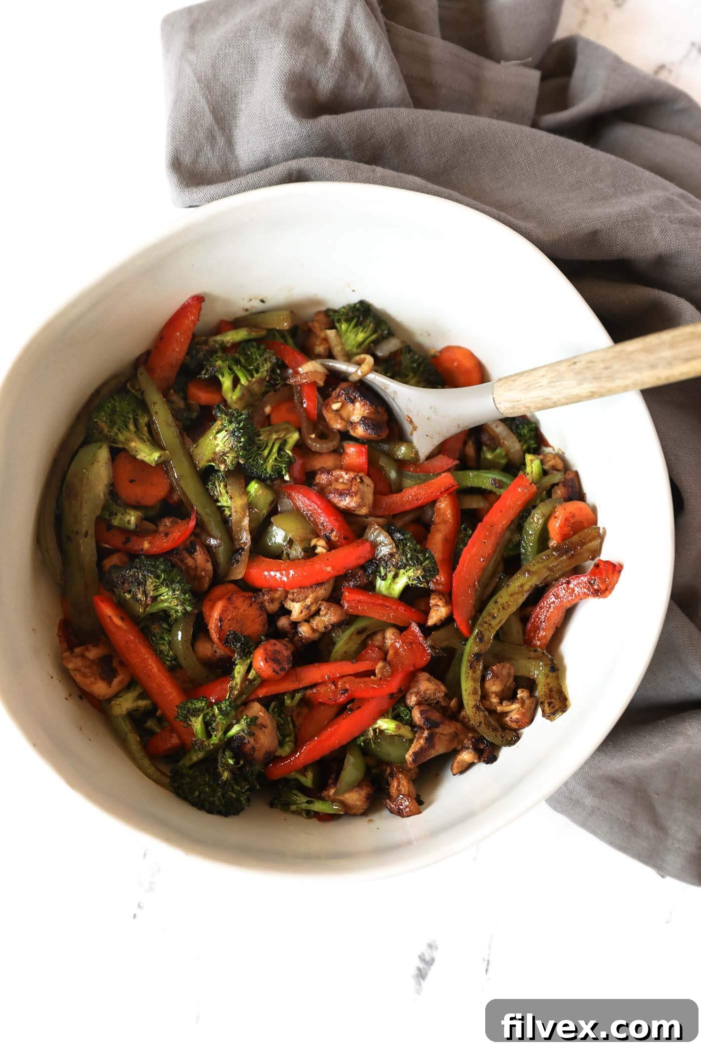 An overhead image of chicken stir fry in a large serving bowl with a serving spoon. 