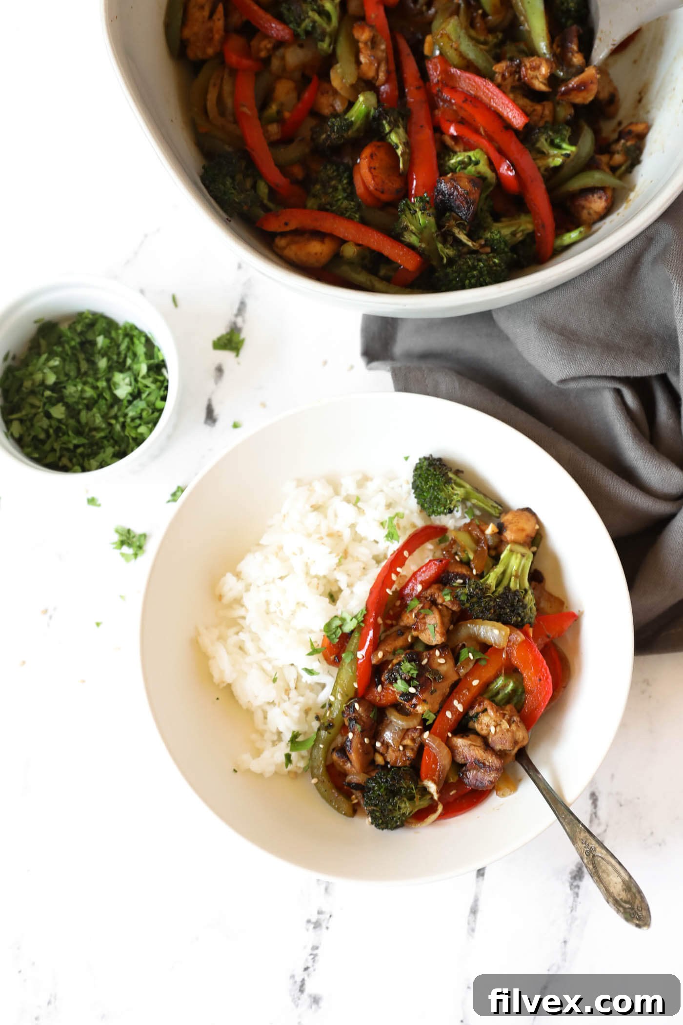 Overhead image of a bowl with rice and stir fry with chopped cilantro sprinkled on top. Large serving bowl with extra stir fry and small ramekin of chopped cilantro on the side.