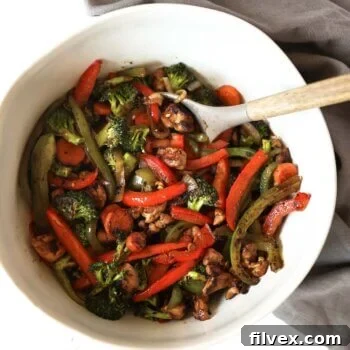 An overhead image of chicken stir fry in a large serving bowl with a serving spoon.
