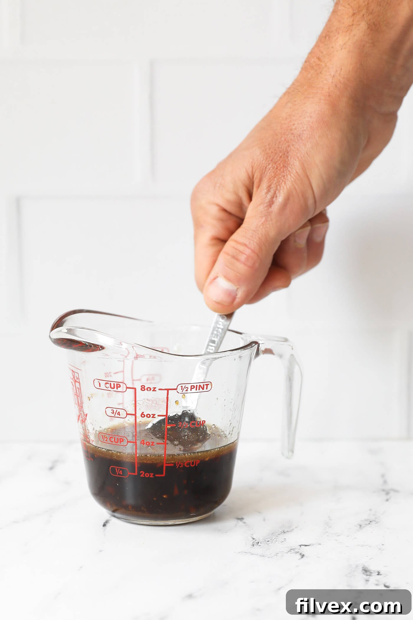 A hand is mixing sauce in a measuring jar.