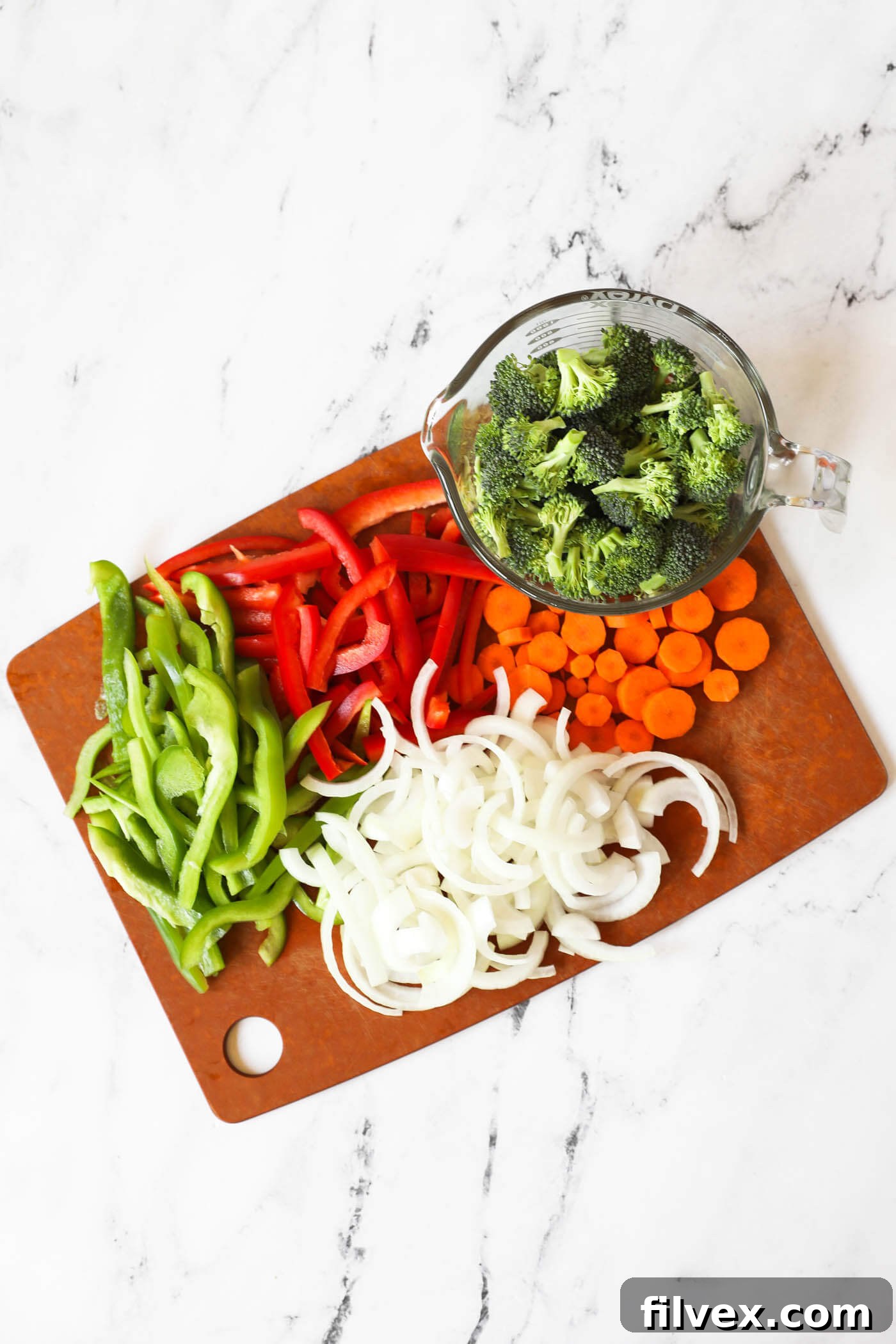 Chopped green and red bell pepper, onion, carrots and broccoli florets on a cutting board.
