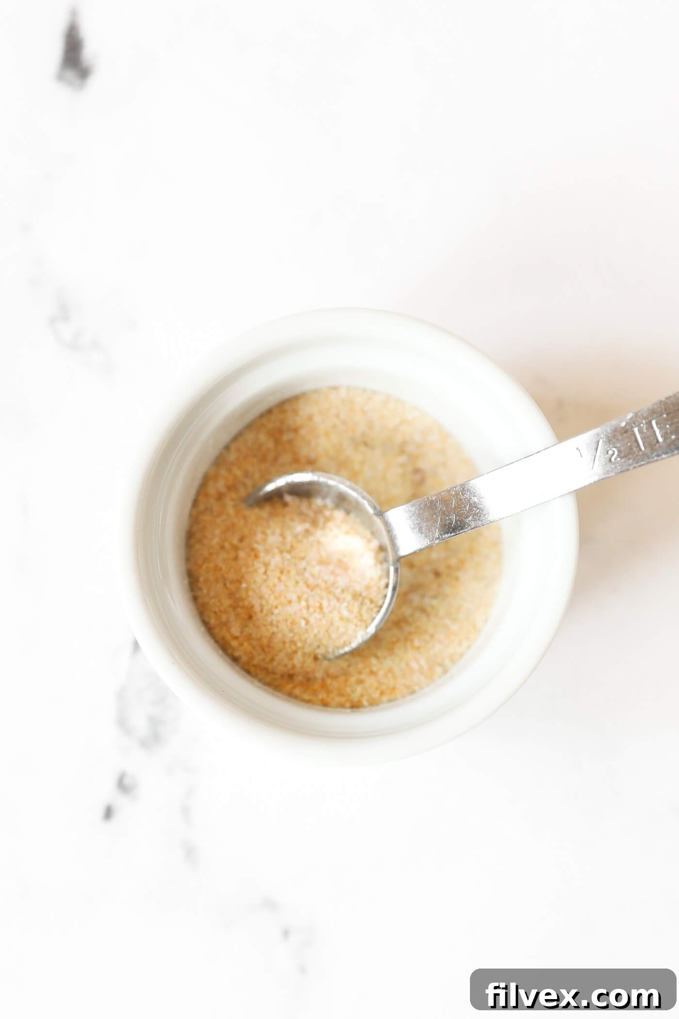 A small ramekin with seasonings and a measuring spoon.