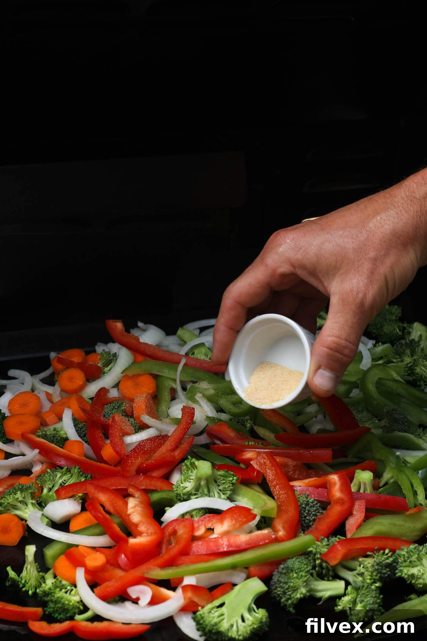 Chopped vegetables cooking on a griddle alongside chicken.