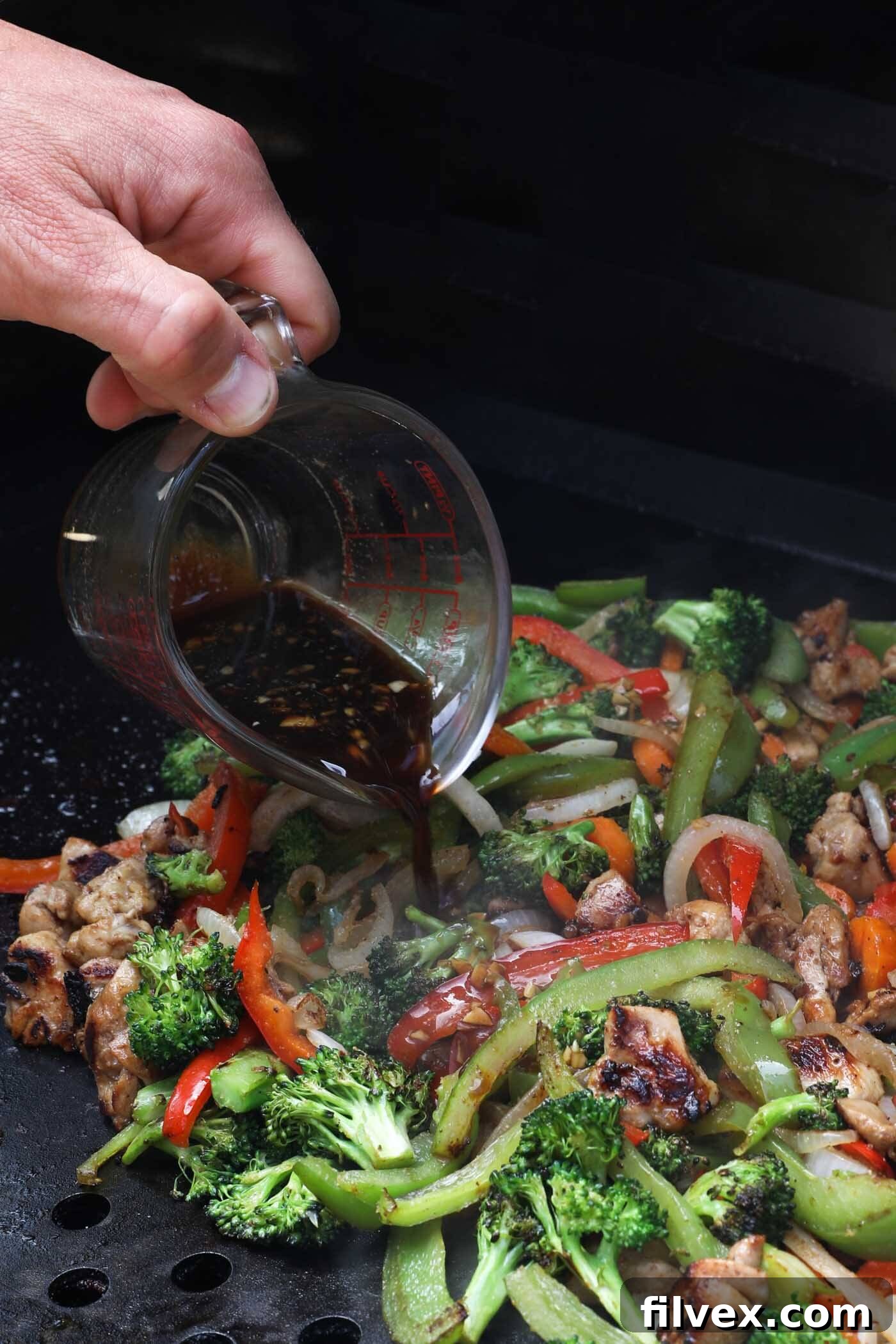 The remaining stir fry sauce being poured over the cooked chicken and vegetables.