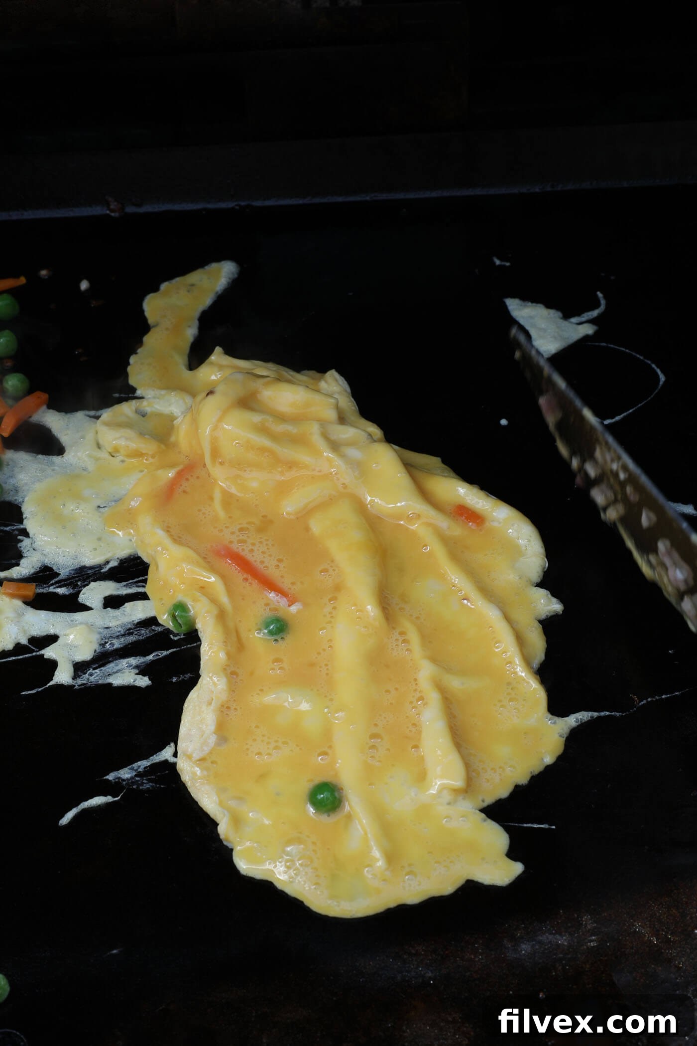 Scrambling egg on the Blackstone griddle in a separate area, cooking quickly until firm.