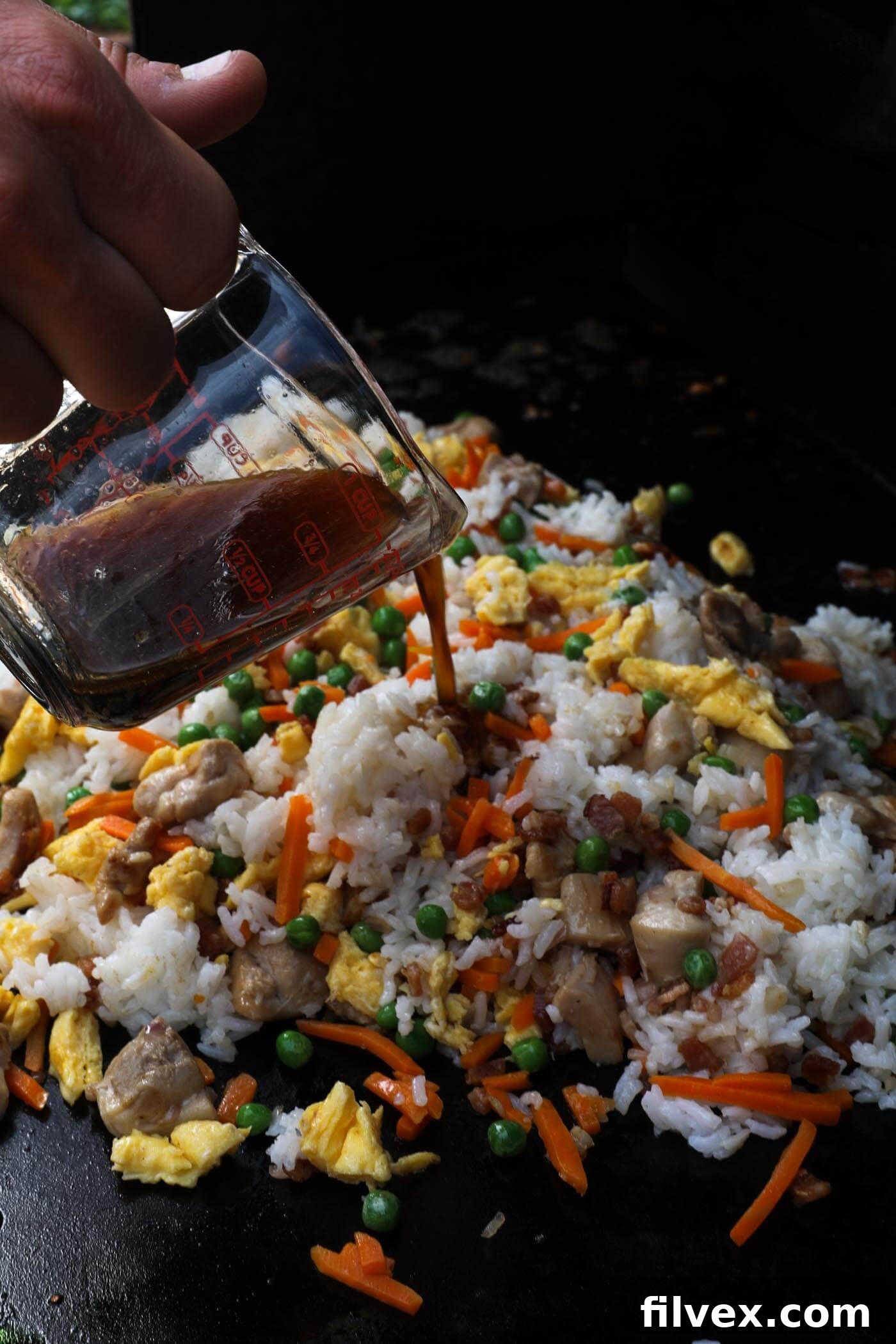 Pouring the remaining sauce over the fried rice mixture on the griddle, ensuring even coating.