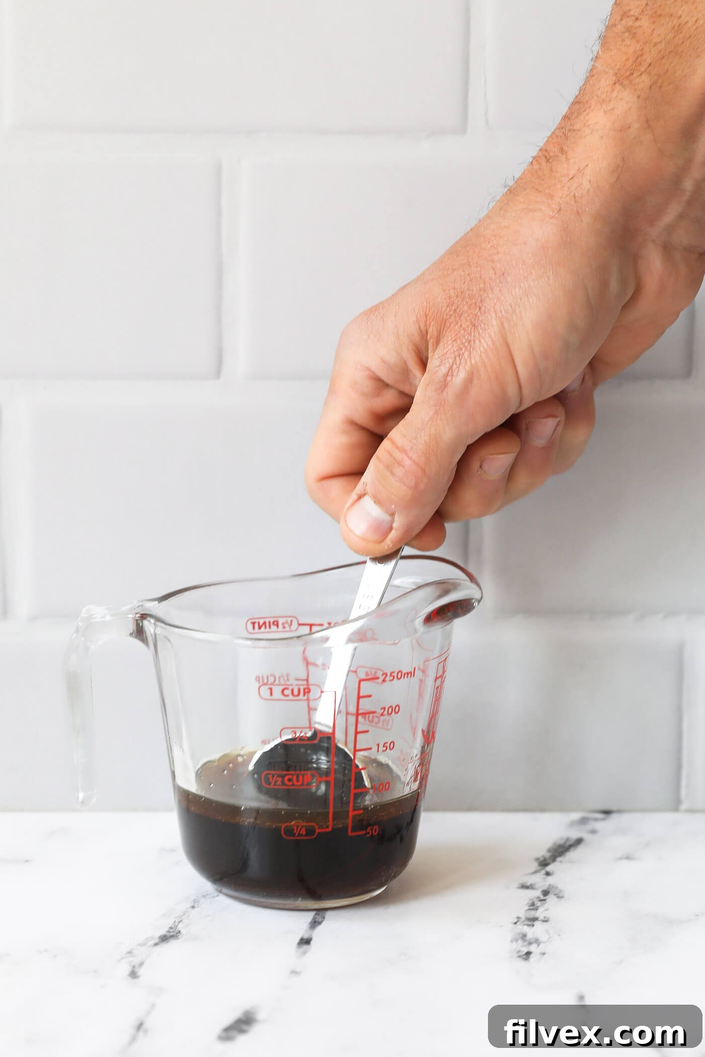 A hand mixing sauce up in mixing jar with a tablespoon, showing the blend of ingredients.
