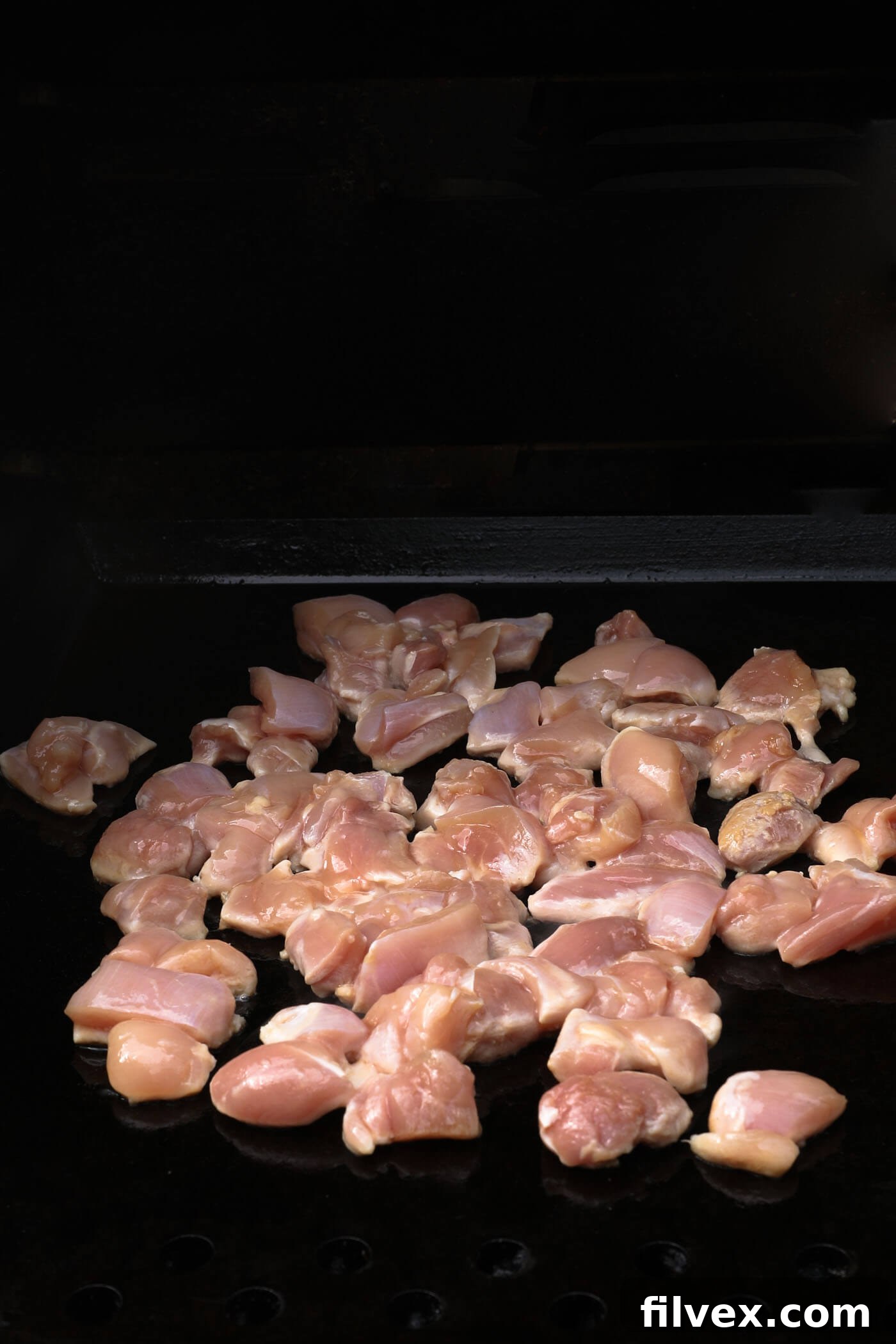 Sliced raw chicken cooking on a hot Blackstone griddle, starting to brown and sizzle.