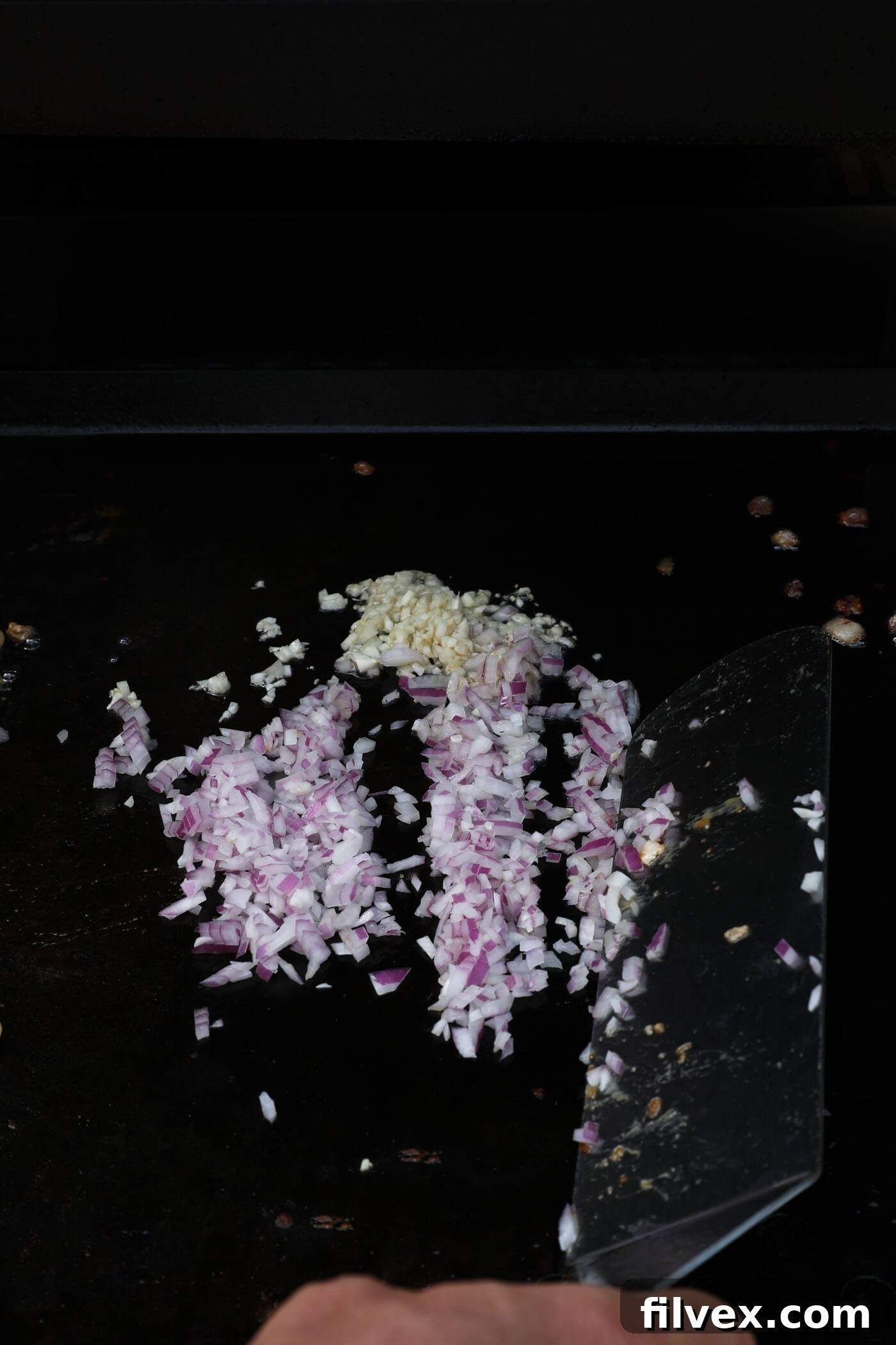 Shallot and garlic cooking on a Blackstone griddle, becoming fragrant and translucent.