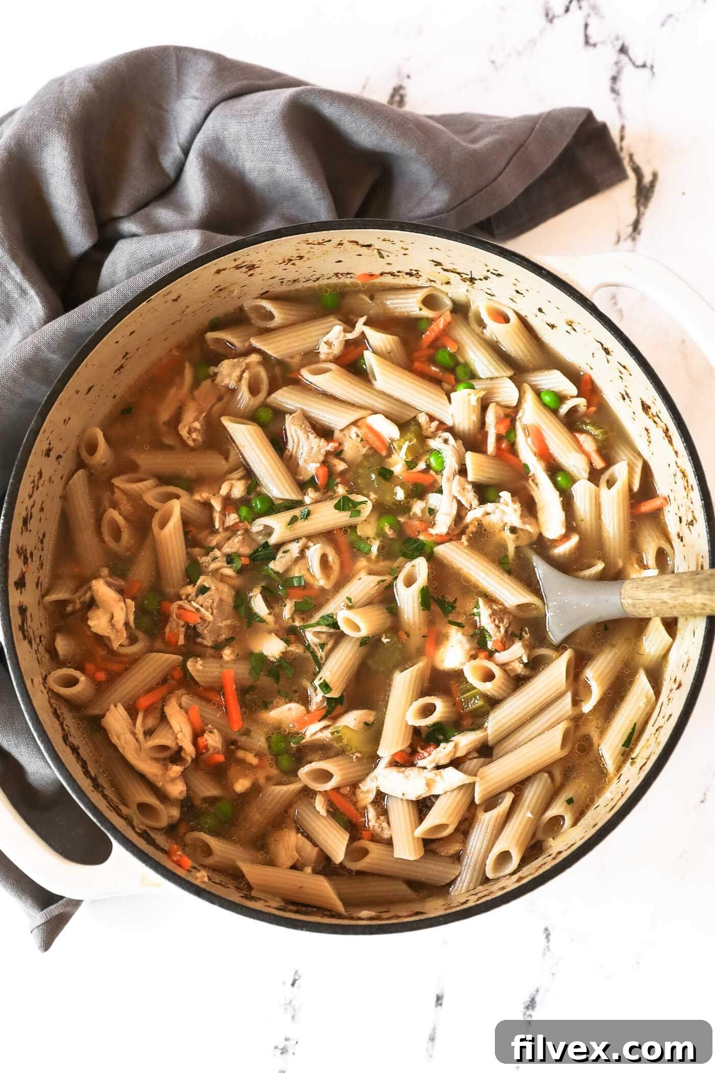 Overhead shot of a large Dutch oven filled with homemade chicken noodle soup, garnished with fresh parsley and a serving spoon, inviting a warm and comforting feel.