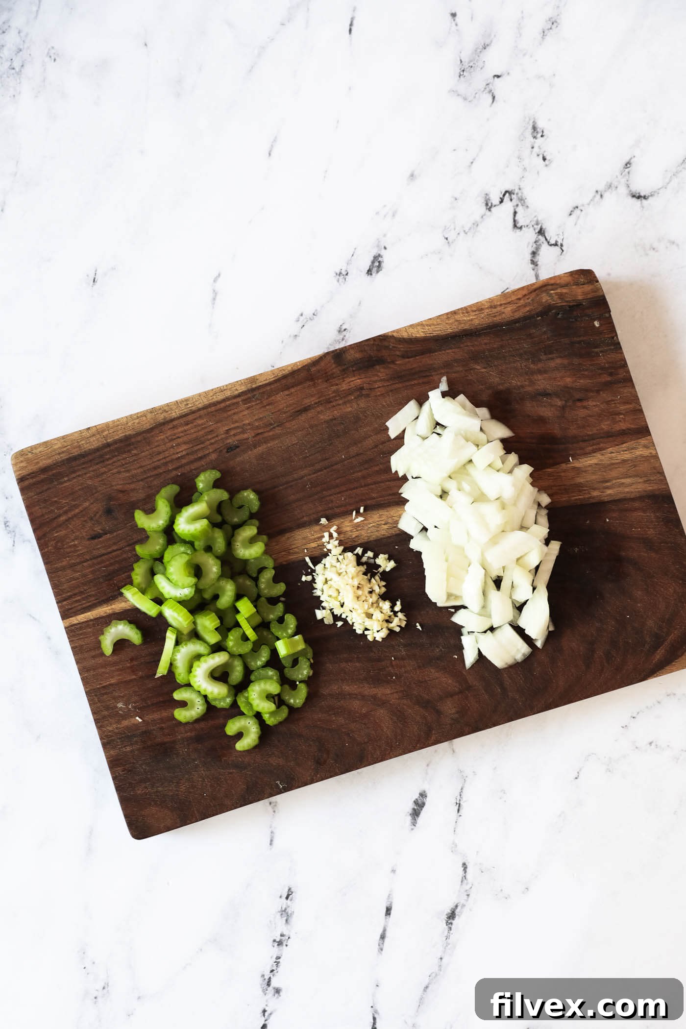 Diced onion and celery with minced garlic neatly arranged on a cutting board, ready for the soup base.