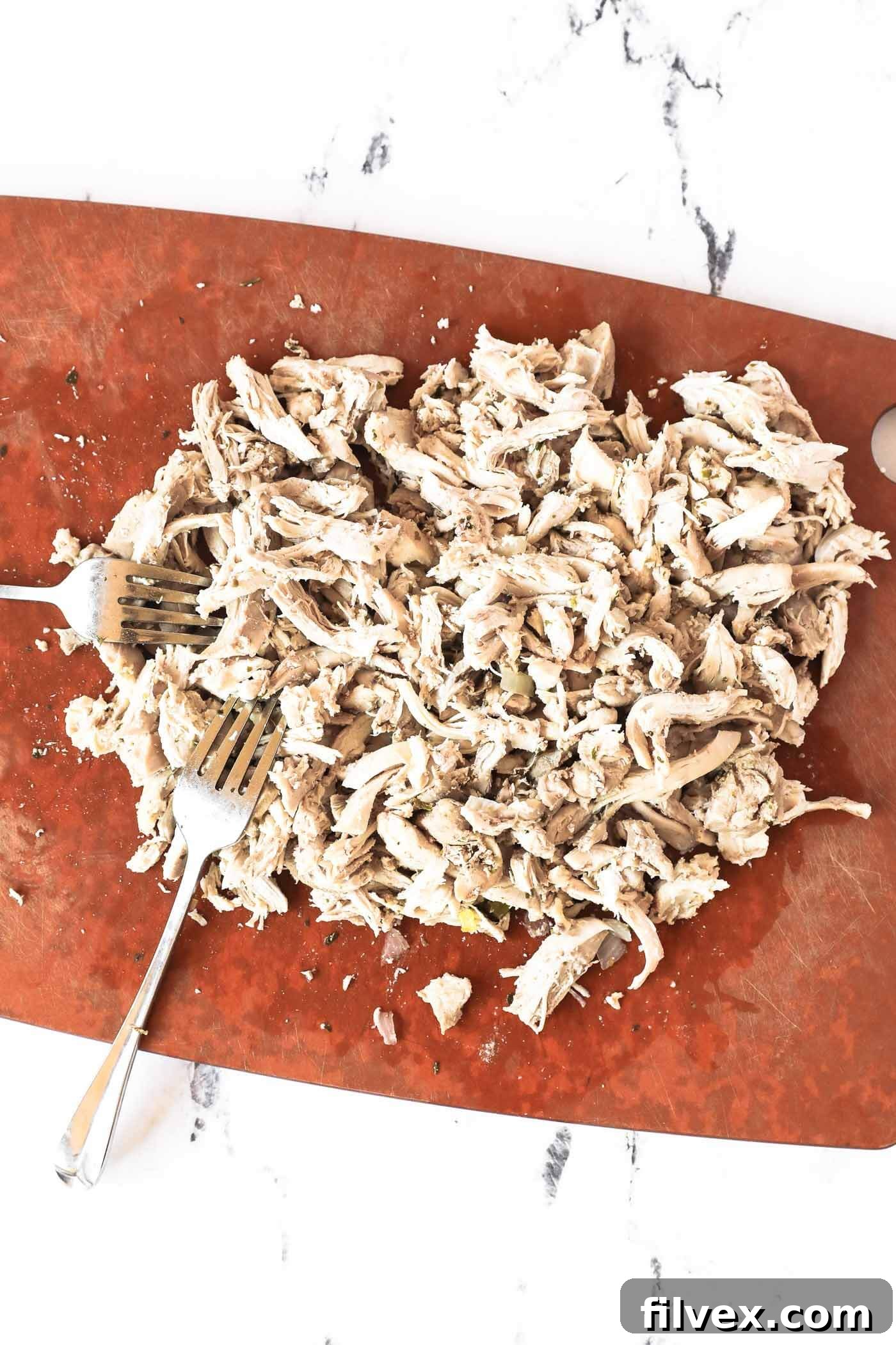 Tender, shredded chicken resting on a cutting board, ready to be added back into the soup.