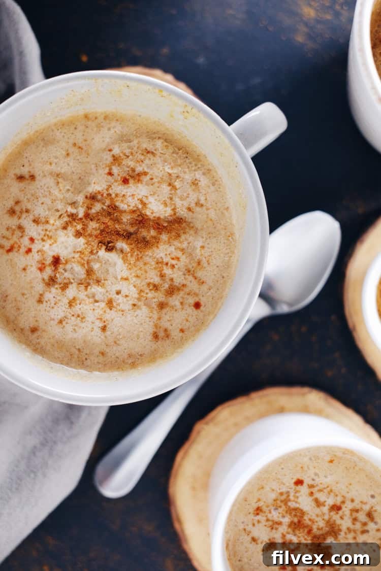 Three mugs of Spiced Pumpkin Coconut Cider, decorated with spices and cinnamon sticks, ready to be enjoyed.