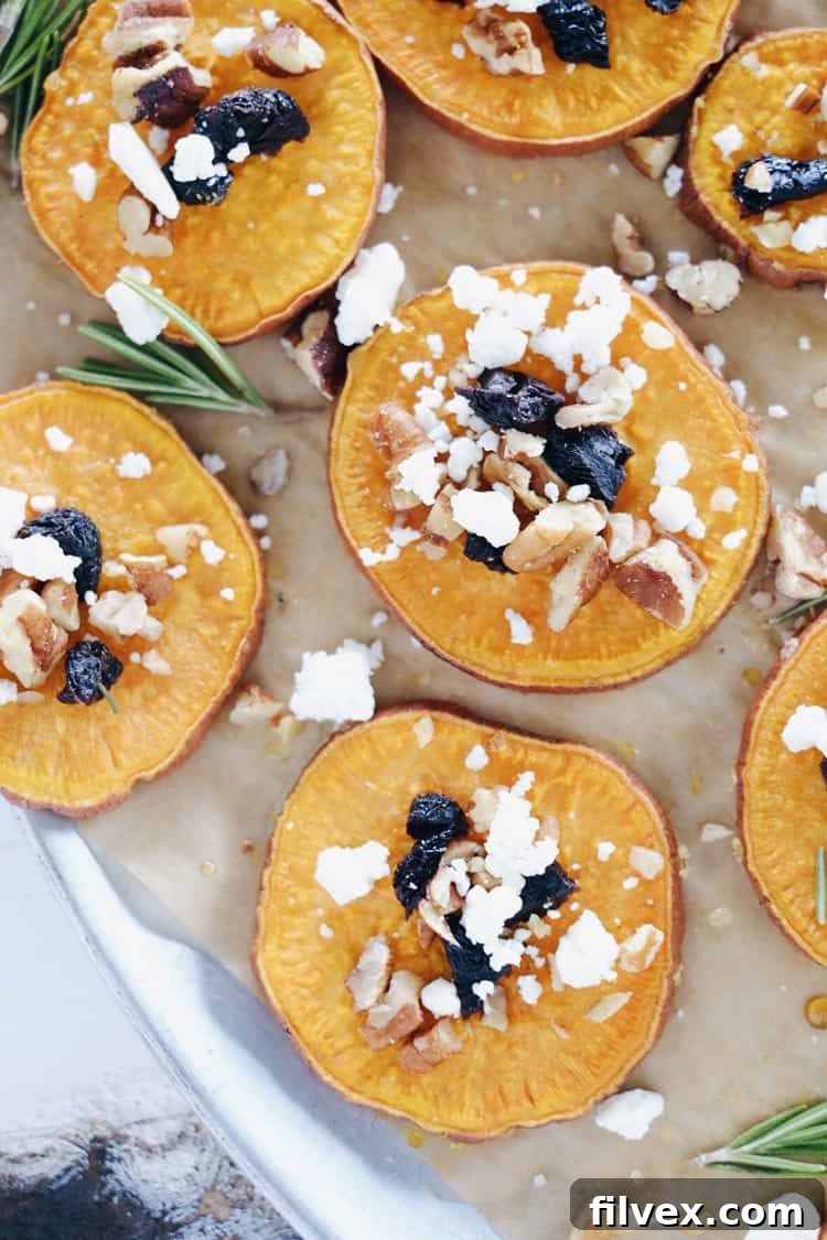 Elegantly arranged roasted sweet potato bites garnished with goat cheese, dried cherries, and pecans, ready for a holiday feast.